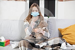 Flu, cold and treatment at home concept. Cute sick teen girl in protective face mask, sitting on sofa at home, under