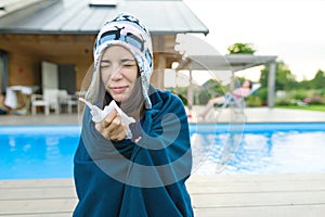 Flu, colds in the summer. Girl in a knitted hat with plaid with handkerchief sneezes, wipes her nose. Background nature, pool, gir