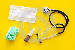 Flu drops. Running nose concept. Wrinkled napkin near stethoscope and face mask on yellow background top view