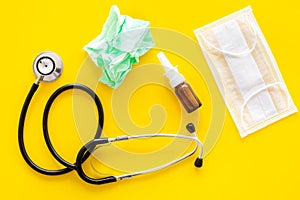 Flu drops. Running nose concept. Wrinkled napkin near stethoscope and face mask on yellow background top view