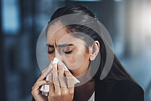 The flu germs have found their way to her. a young businesswoman blowing her nose in an office.