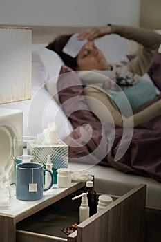 Flu medicines on bedside table ill woman