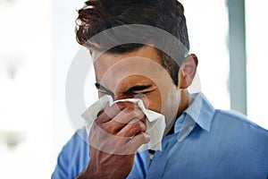 Flu season is on its way. a young businessman blowing his nose at work.