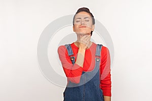 Flu symptom. Portrait of sick unhealthy girl in casual denim overalls touching painful neck, suffering sore throat