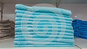 Fluffy bathing towels in blue and cyan colors stacked on shelf for sale in a store