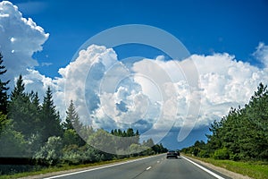 Fluffy clouds over highway. Driving on country road in summer day.