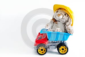 Fluffy, cuddly, cute little rabbit bunny toy in yellow helmet in truck toy on white background with copy space