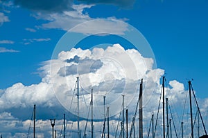 Fluffy cumulous clouds, deep blue sky and multiple masts