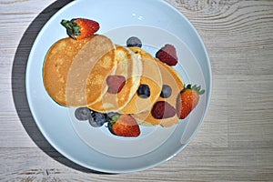 Fluffy japanese pancakes with berries isolated on white wooden table.