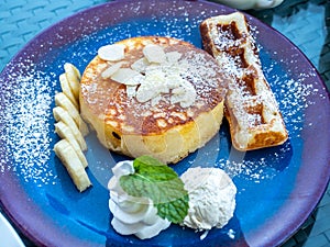 Fluffy pancake with a piece of waffle serve with banana, cream, syrup and honey