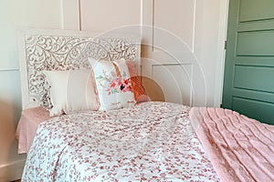 Fluffy pillows against headboard of bed with floral bedsheet and pink blanket