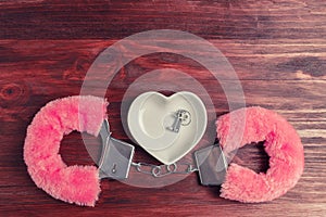 Fluffy pink handcuffs and a ceramic saucer in the shape of a heart, wherein lie the keys