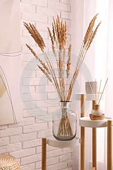 Fluffy reed plumes near white brick wall indoors. Interior element