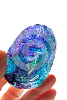 Fluorite crystal hand held in sunlight with purple, blue and turquoise colors