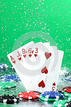 Flush poker combination under the water drops and falling poker chips against green background. Online gambling. Betting. Gambling