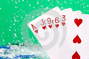 Flush poker combination under the water drops and falling poker chips against green background. Online gambling. Betting. Gambling