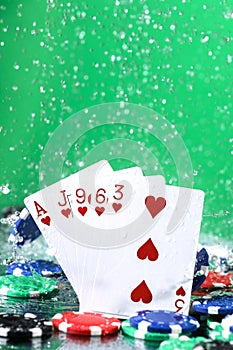 Flush poker combination under the water drops and falling poker chips against green background. Online gambling. Betting. Gambling
