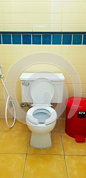 Flush toilet with red trash can on yellow tile in bathroom, restroom. Public washroom and clean room.