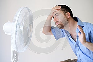 Flushed man feeling hot in front of a fan