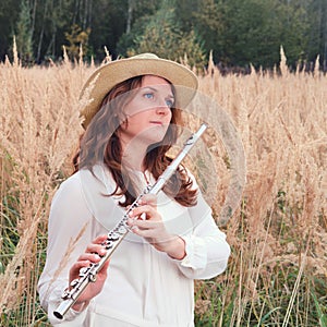 A flute player holds a concert flute while standing in the tall autumn grass. A musician with a wind instrument in the tall grass