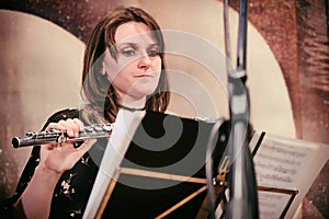 The flutist looks at the notes. Woman on stage with a flute. The musician looks at the notes on the music stand