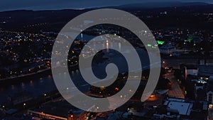 Fly above city in evening. Aerial view of river flowing through night town with street lights. Limerick, Ireland