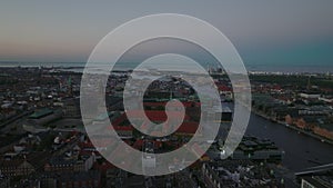 Fly above historic city centre at twilight. Aerial panoramic view of town development and sea in distance. Copenhagen