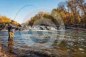 Fly fisherman catching a fish in the mountain river.