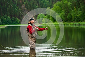 Fly fishing angler makes cast while standing in water