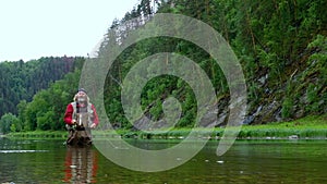 Fly fishing. A mountain river. An elderly man with long hair and a Santa Claus beard stands in the water and holds a fishing rod