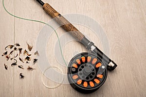 Fly fishing reel, rod, and flies on a light wood background