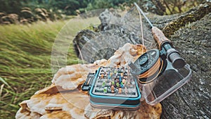 Fly fishing rod and box with flies on the background of a forest river