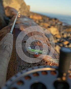 A fly fishing rod and flies for fly fishing lie on the sea rocks at sunset.