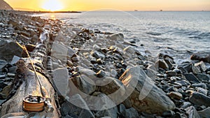 A fly fishing rod and an open fly fishing box lie on the sea rocks at sunset.