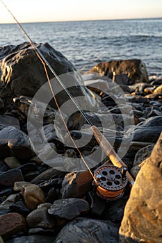A fly fishing rod on the sea rocks at sunset.