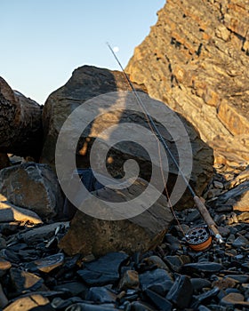 A fly fishing rod on the sea rocks at sunset.