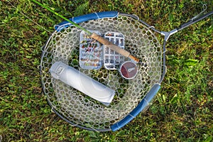 Fly fishing tackle. Tackle box with flies, rod, reel and thermo water bottle on fishing landing net