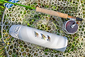Fly fishing tackle. Flies on thermo water bottle, rod, reel in fishing landing net