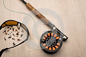 Fly fishing tackle,  sunglasses, fishing  rod, reel and flies on a light wood background with copy space
