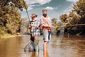 Fly fishing for trout. Father with son on the river enjoying fishing holding fishing rods.