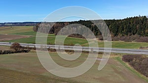 Fly over autobahn near forest with town on horizon.Aerial video of autobahn through green meadow and forest