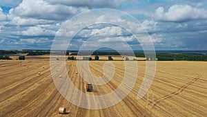 Fly over a golden wheat field. A tractor with a baler collects straw into bales.