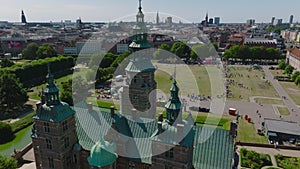 Fly over Rosenborg castle. Revealing people watching sport event in park. Buildings in city in background. Copenhagen