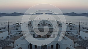 Fly over traditional houses on Milos Island, Greece. Aerial view of sea bay at dusk. Abstract computer effect digital