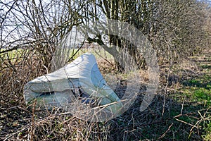 Fly tipping image of an old used mattress dumped in hedges