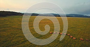 Flying above green field with hay stacks,aerial view of forest and hills. Russia