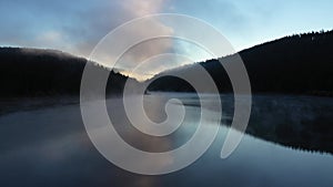 Flying above misty mountain lake at dawn. Aerial view by drone