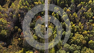 Flying above a white car driving on colorful autumn forest road. Aerial view