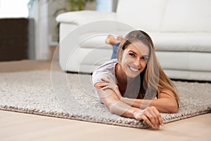 Flying away on my magic carpet. Portrait of a woman smiling at the camera while lying on her living room floor.