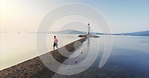 Flying backwards, aerial portrait of young sportsman running along the sandbank